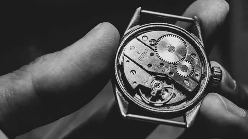Close-up of vintage watch caliber plates and precision gears held under workshop light
