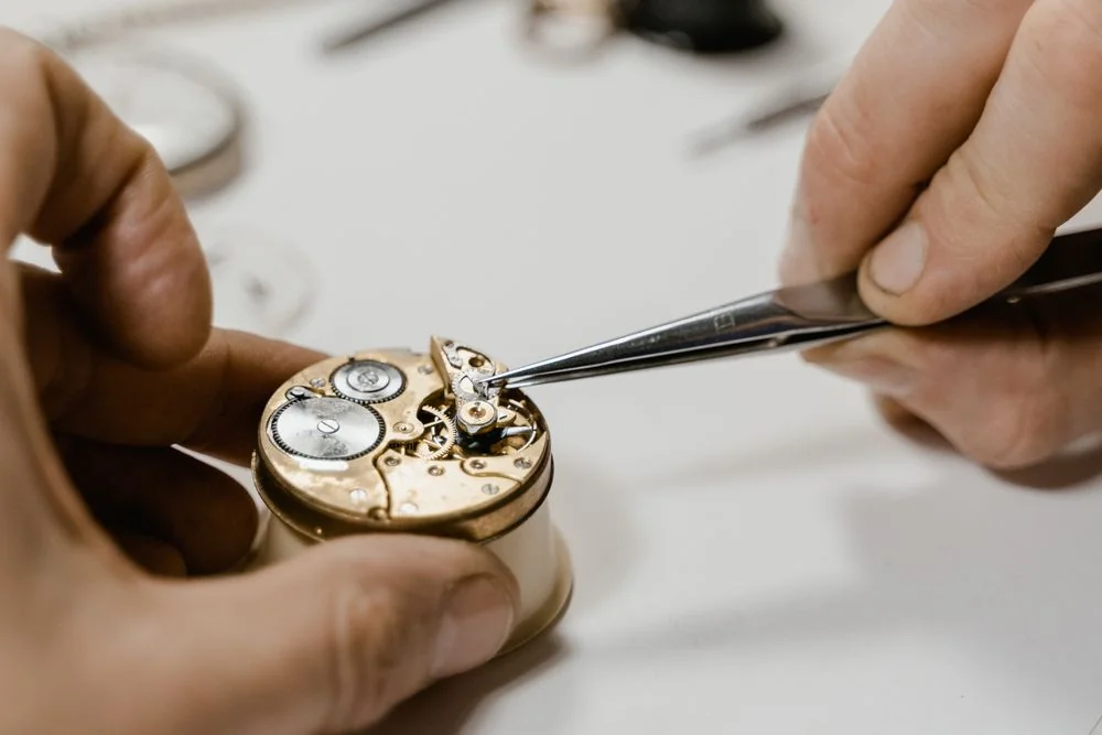 Skilled watchmaker hands manipulating fine movement components with precision tweezers